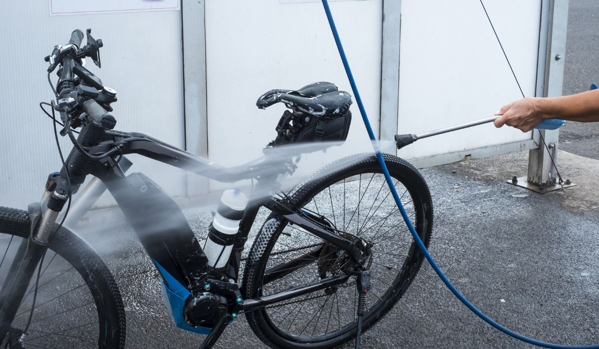 Man washing his electric bicycle at the service station. High pressure pump