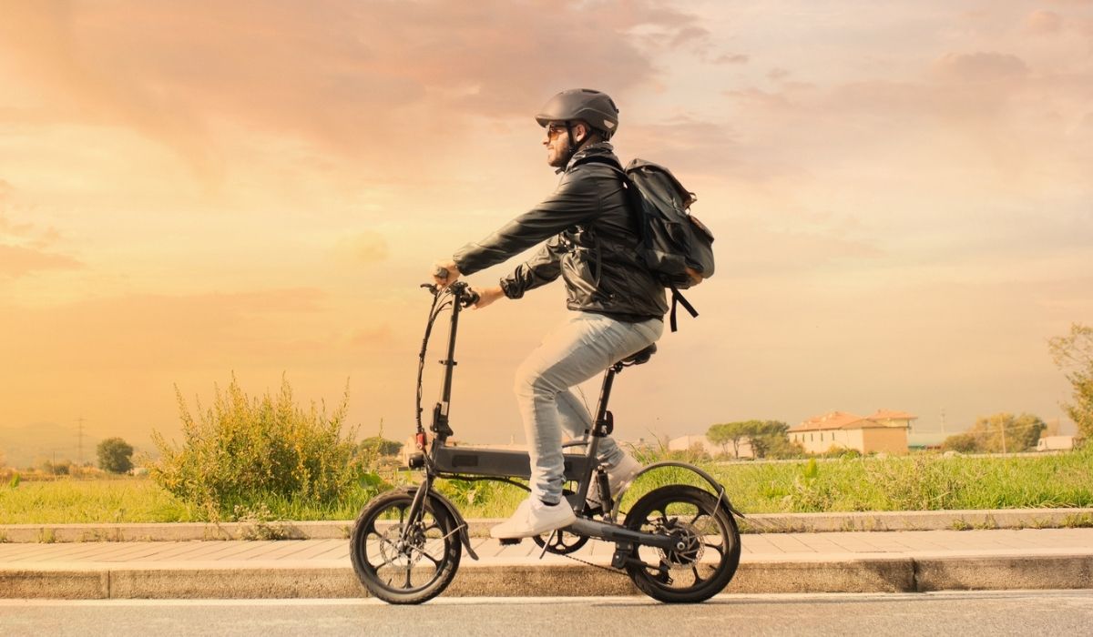 Smiling man with helmet and his electric bicycle at sunset