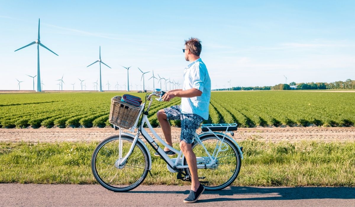 Young man electric green bike bicycle by windmill farm