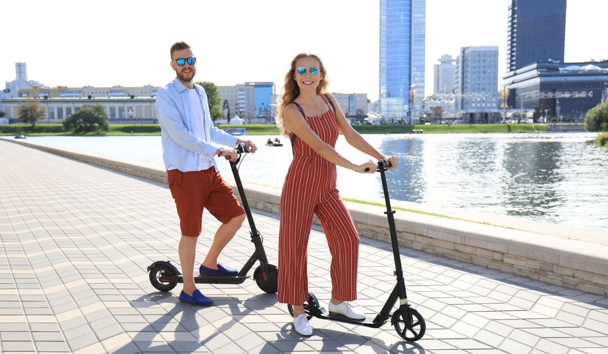 Lovely couple having fun driving electric scooter along the city promenade