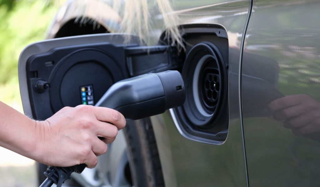 Female hand inserts plug for charging electric car closeup