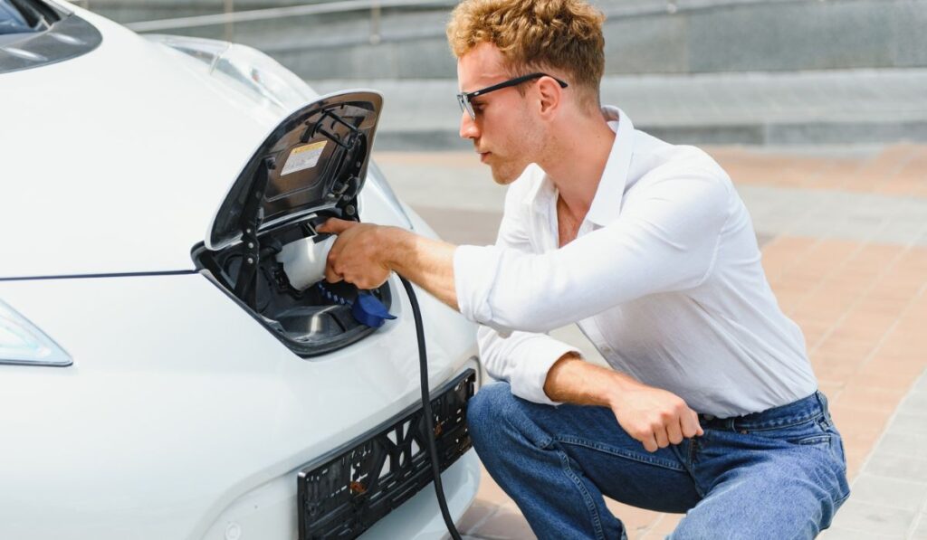Stylish man inserts plug of the charger into the socket of electric car close-up